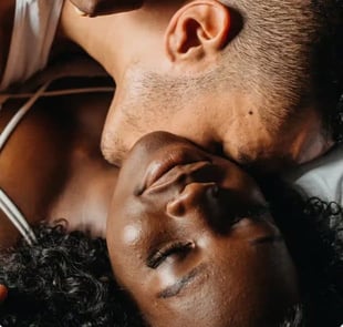 Photo of a young man kissing a young woman's neck while the woman closes her eyes and smiles 