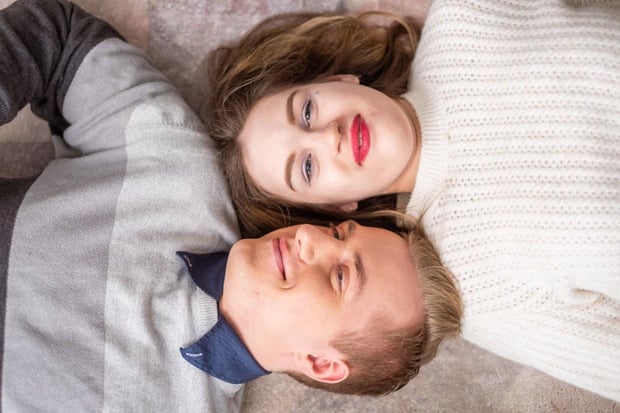 Photo of a young couple lying on a bed with their heads side by side and both smiling