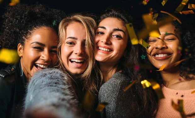 Stock image of four young women smiling and taking a selfie with confetti falling around them 