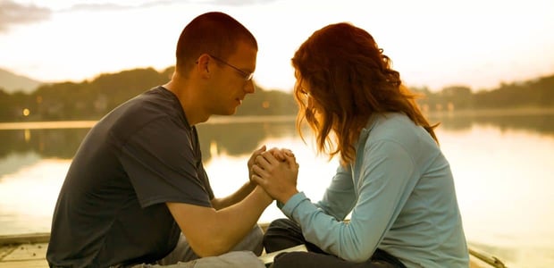 Couple clasping hands in front of a lake.