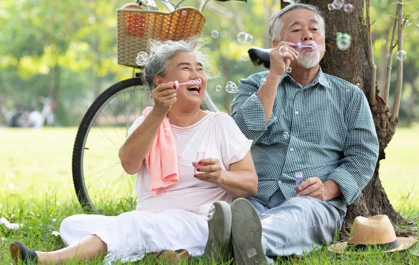 Old couple laughing and blowing bubbles against a tree together